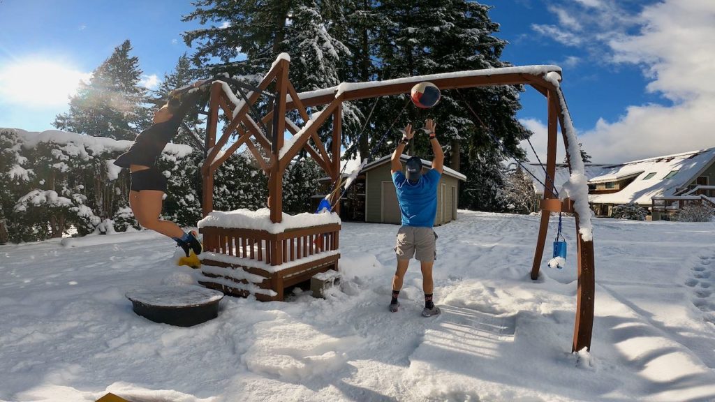 Joe tossing a wall ball against the swing set in the backyard workout