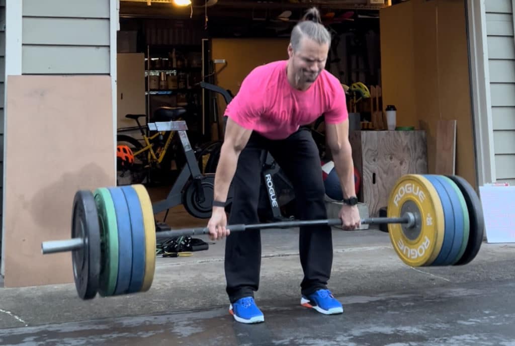 Joe deadlifting a Rogue barbell with Rogue bumper plates outside of garage